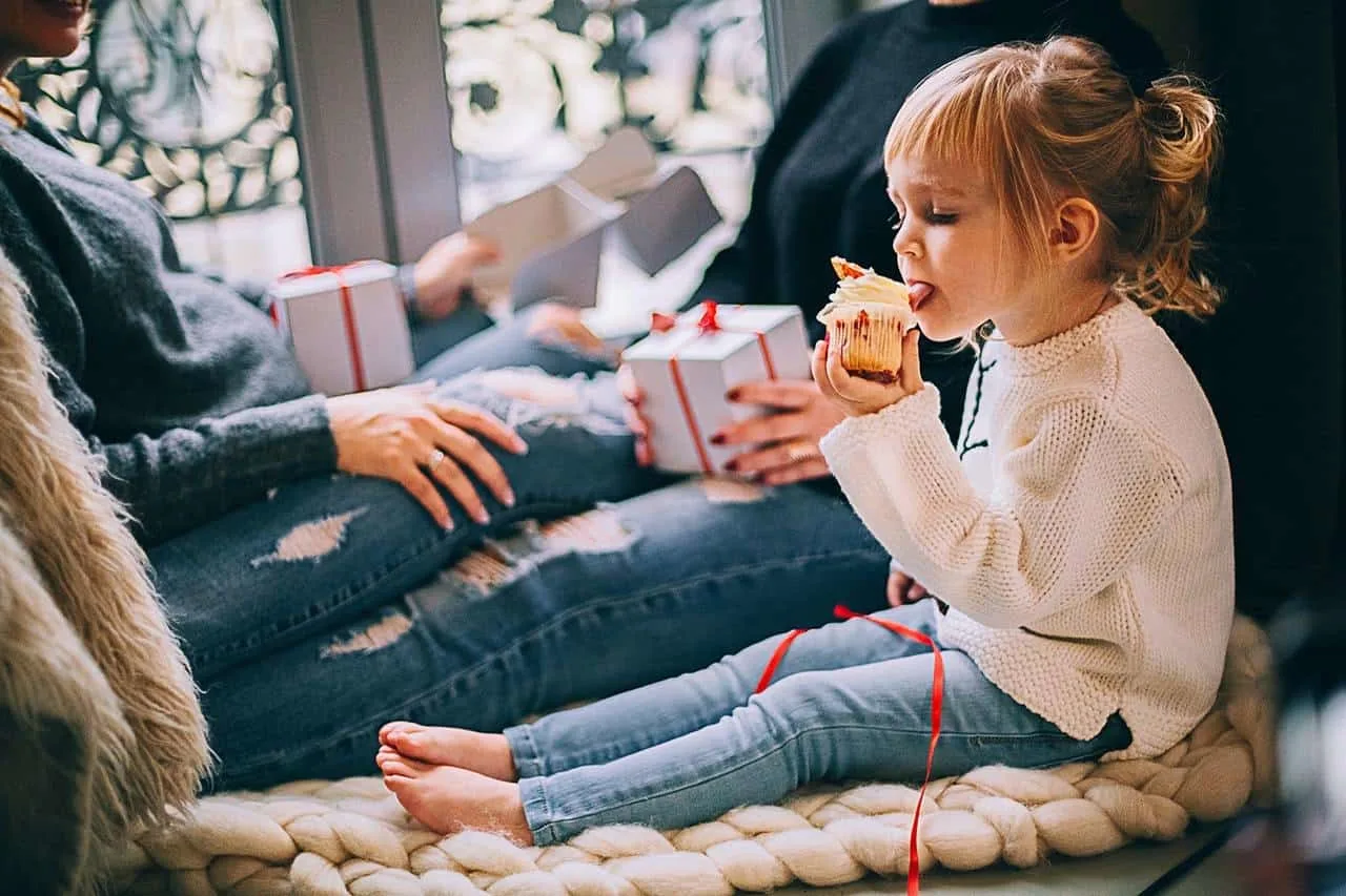 girl-eating-cupcake-while-sitting-beside-woman - try making cupcakes as an advent activity to celebrate Jesus's birth