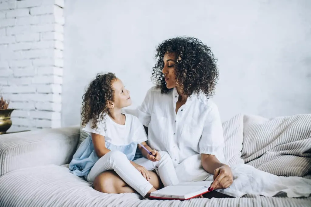 Mom and daughter sitting on a bed writing in a journal