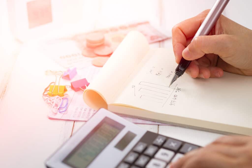 a woman writing on a paper while using a calculator