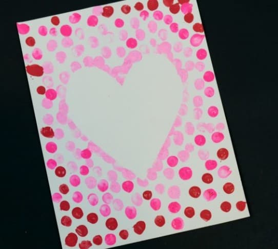 A piece of paper with painted thumbprints all over it, except for a heart in the middle