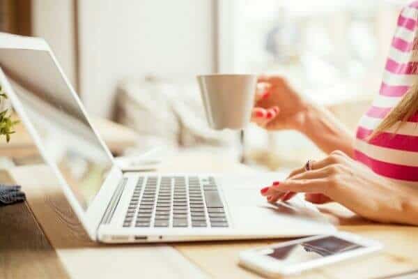 a woman uses a laptop and holds a cup