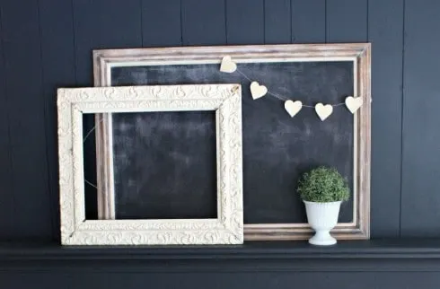 A simple paper heart garland is strung over on empty wooden picture frame against a black wall