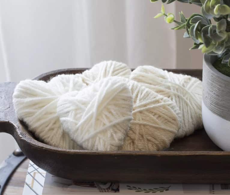 Cardboard hearts wrapped in white yarn look classy sitting in a wooden bowl on a kitchen counter, making it a perfect understated Valentines day decoration