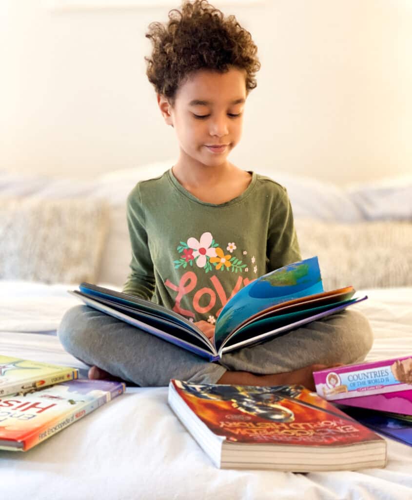 a girl reads on a bed - choosing a literature-based program that kids love can improve the family dynamic in your homeschool