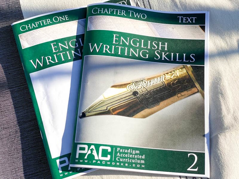 Two workbooks lying on a cloth: English Writing Skills Textbook and Activity Book by Paradigm Accelerated Curriculum