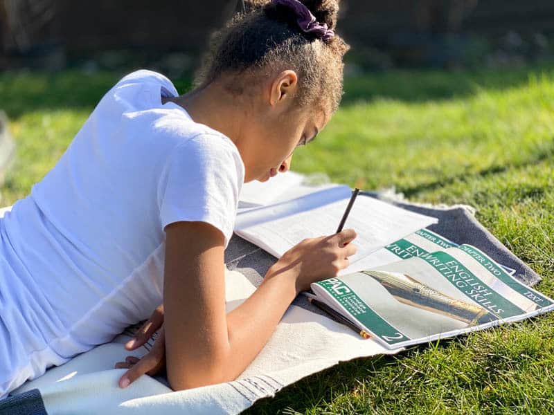 A teenage girl lies on the ground outside studying