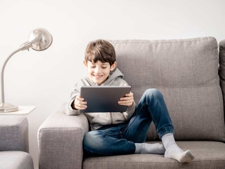 a little boy sitting on a couch using a tablet