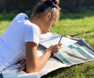 A teenage girl studies a high school English curriculum book while sitting on wooden steps outside