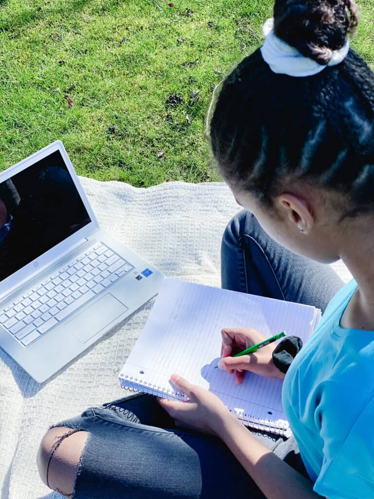 A girl writes and works on a laptop outside. Mr D Math's Advanced writing course is the perfect blend of online high school writing course and traditional homeschooling. 