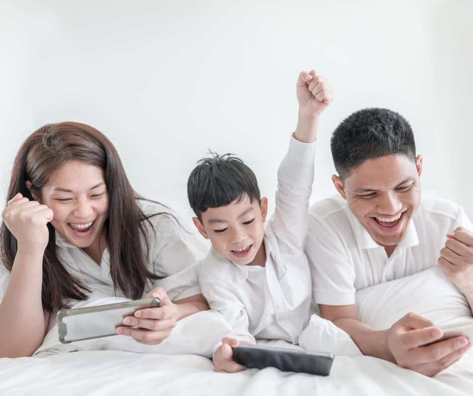 A family lies side-by-side playing on their own devices and laughing. Devices have become ubiquitous; perhaps it's time to unplug. 