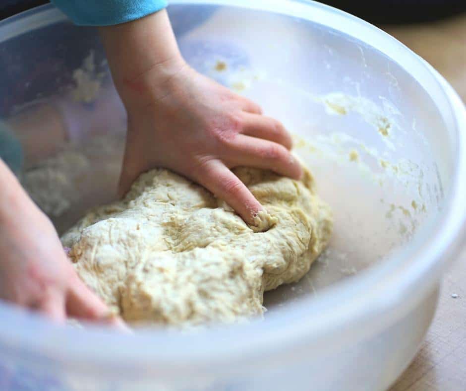 Small hands knead bread dough in a big bowl. Making bread with kids is a great hands-on activity to partake in on National Day of Unplugging. It helps kids connect with their parents, their food, and ancient tradition practiced all over the world.
