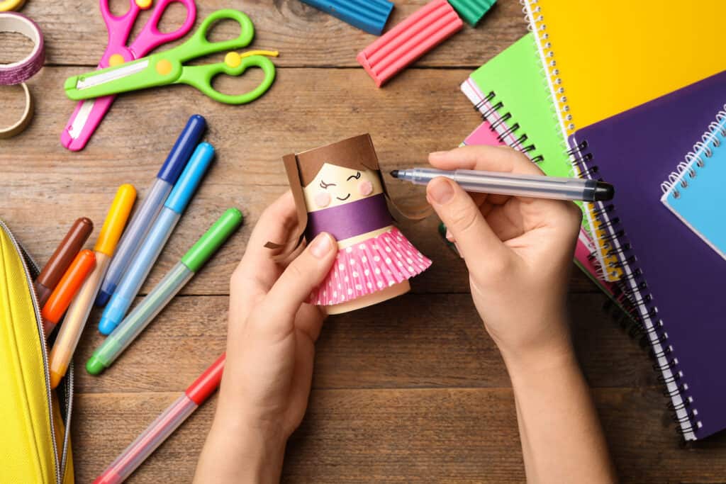 Woman making toy doll from toilet paper hub at wooden table, top view