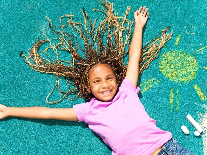 girl playing outside drawing with chalk on a driveway