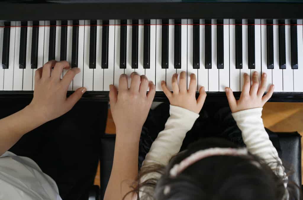 Two sets of hands playing a piano - learn to play piano at home 