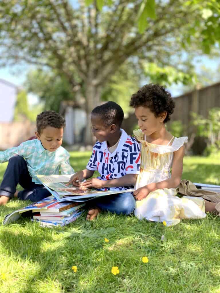three kids look excitedly at a box of books - choosing a literature-based program that kids love can improve the family dynamic in your homeschool