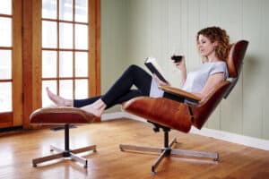 Woman sitting in chair with ottoman in cozy bedroom reading nook