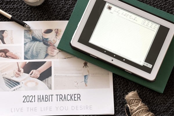 a printed copy of a monthly habit tracker and a digital version on a tablet
