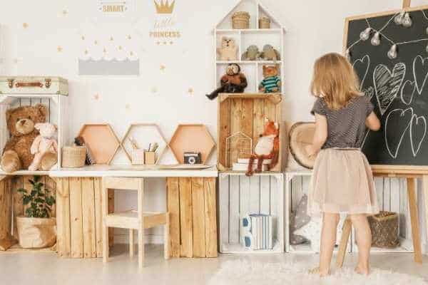 a girl draws on a chalkboard in a room with wooden crate storage