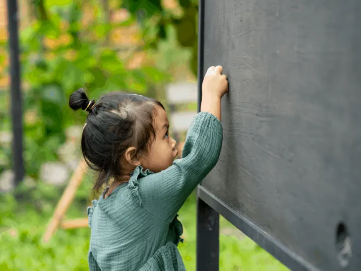 little girl drawing on a backyard chalkboard