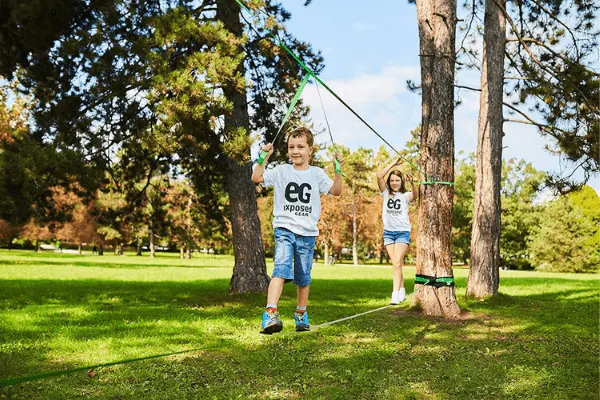 kids walk on a DIY tightrope held between two trees