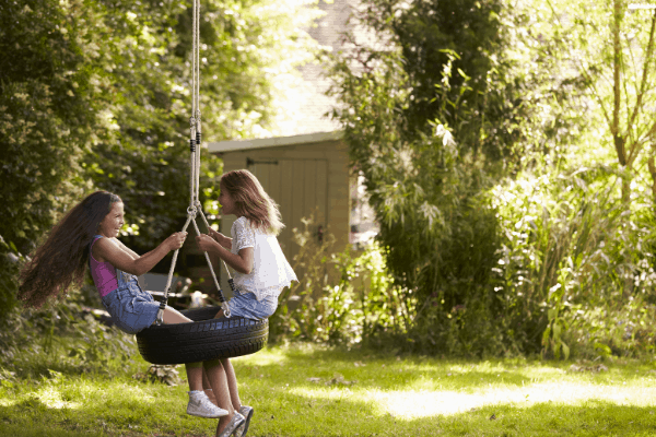 2 girls play on a backyard tire swing - a classic addition for any kid-friendly backyard