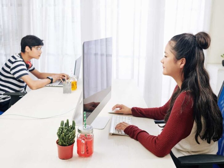 two teenagers work on computers at home