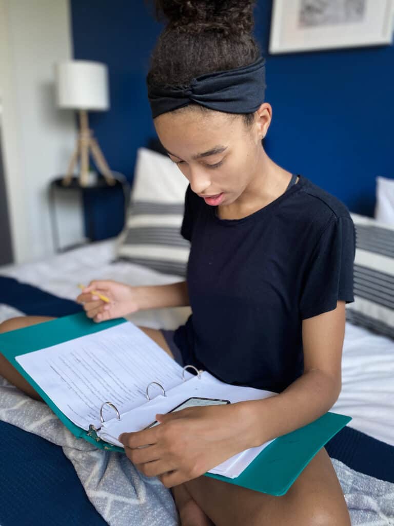 a teenager sits on a bed and does her WriteShop writing assignment