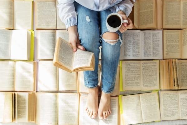 gifts that keep giving | the book lover in your life will cherish a book of the month club subscription | a woman reads in the midst of a sea of books