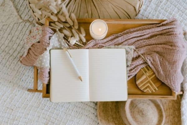 A journal sits open on a tray with a pencil and a candle