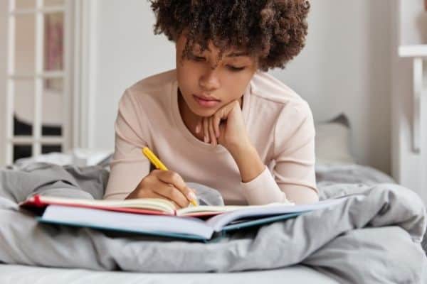 a woman writes in a journal while lying on a bed