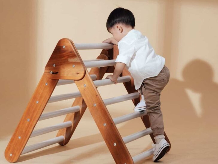 a little boy climbs up a wooden triangle ladder