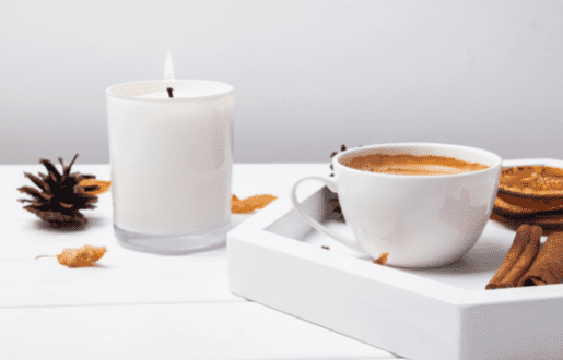 A candle burning beside a cup of coffee