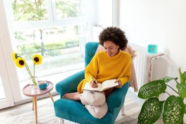 a woman sits in a chair and writes in a journal