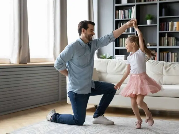 a dad dances with his daughter in a living room