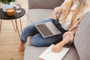 a woman sits on a couch with a laptop and a notebook