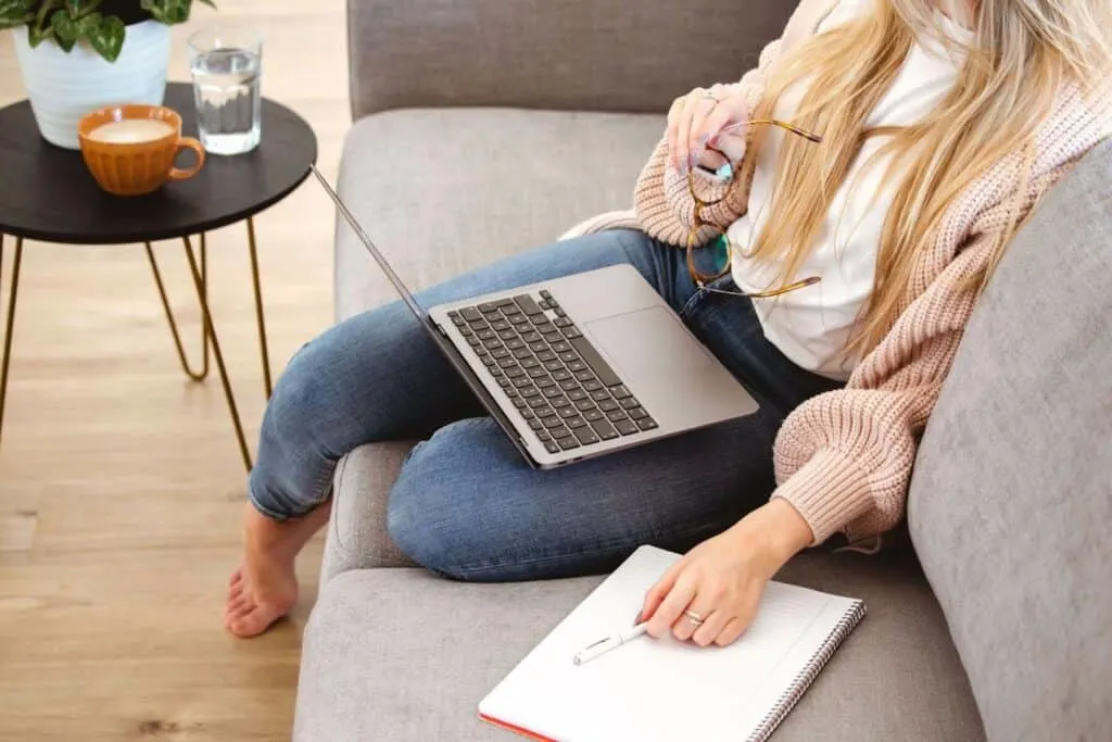 a woman sits on a couch with a laptop and a notebook