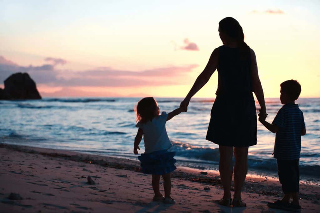 a mother and her children on the beach at sunset