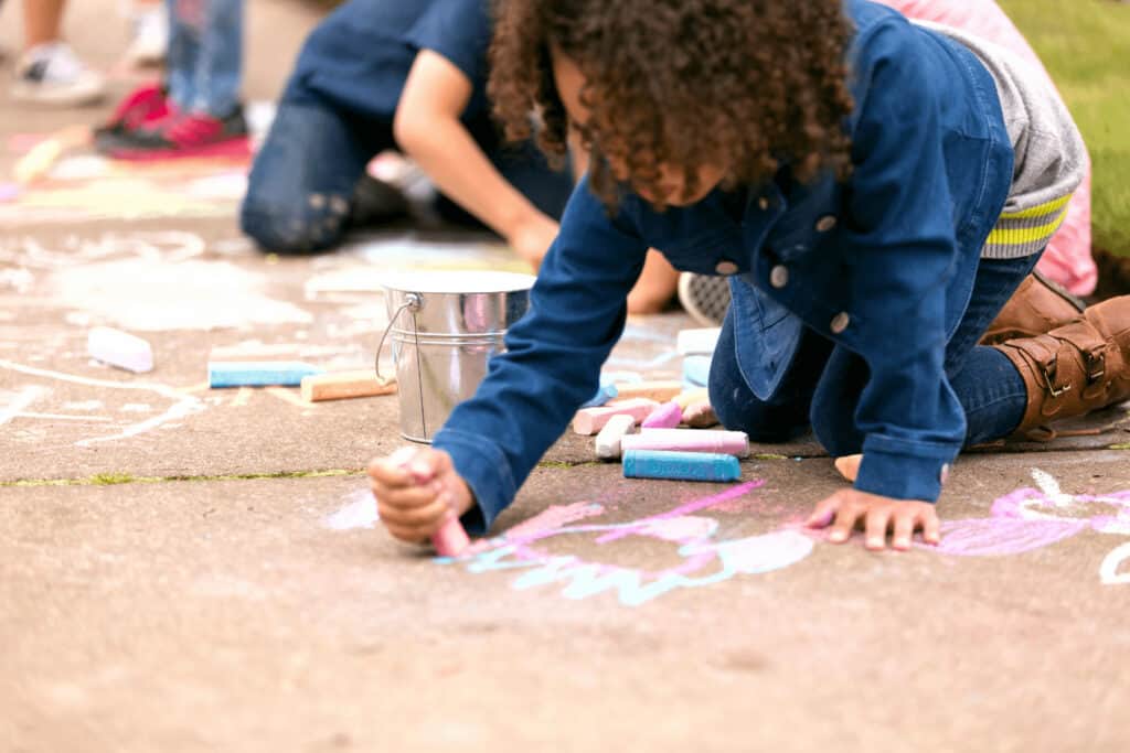 a child draws with chalk on a sidewalk
