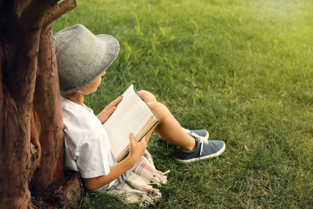 a kid reads outside under a tree