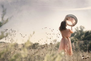 a woman stands in a field and looks at her reflection in an old mirror