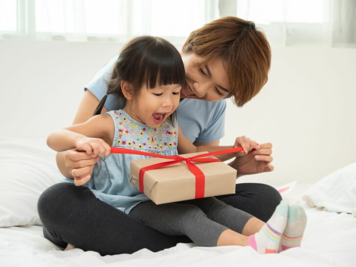 6-year-old christmas gift ideas - a little girls sits on her mom's lap and opens a present