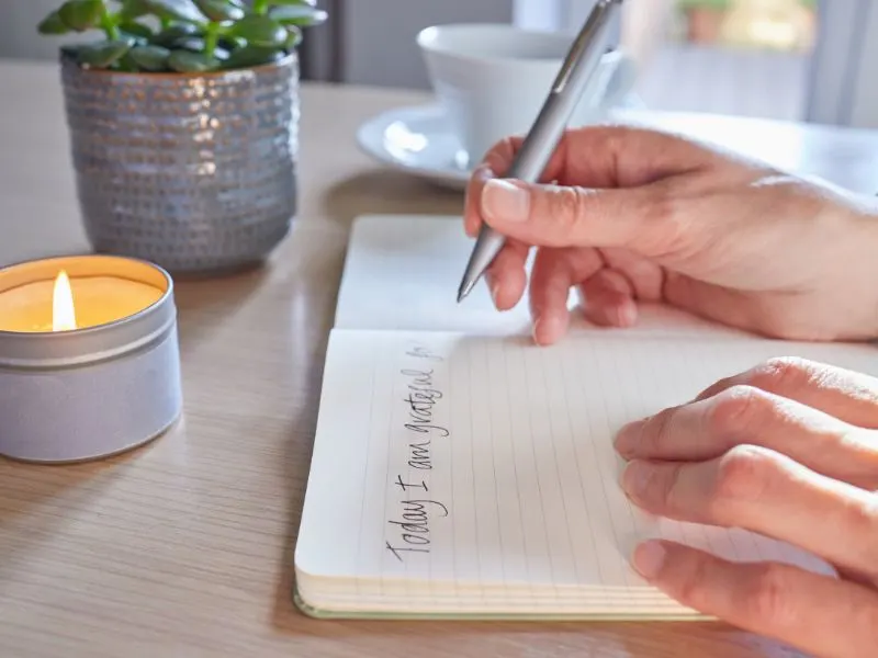 a woman's hand writes in a journal by candlelight